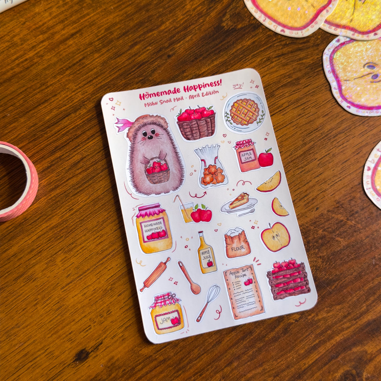 close up of the kawaii sticker sheet from the Mishu Snail Mail April Edition "Homemade Happiness", featuring Mishu the Hedgehog and hand-illustrated apple-themed designs on a wooden surface.