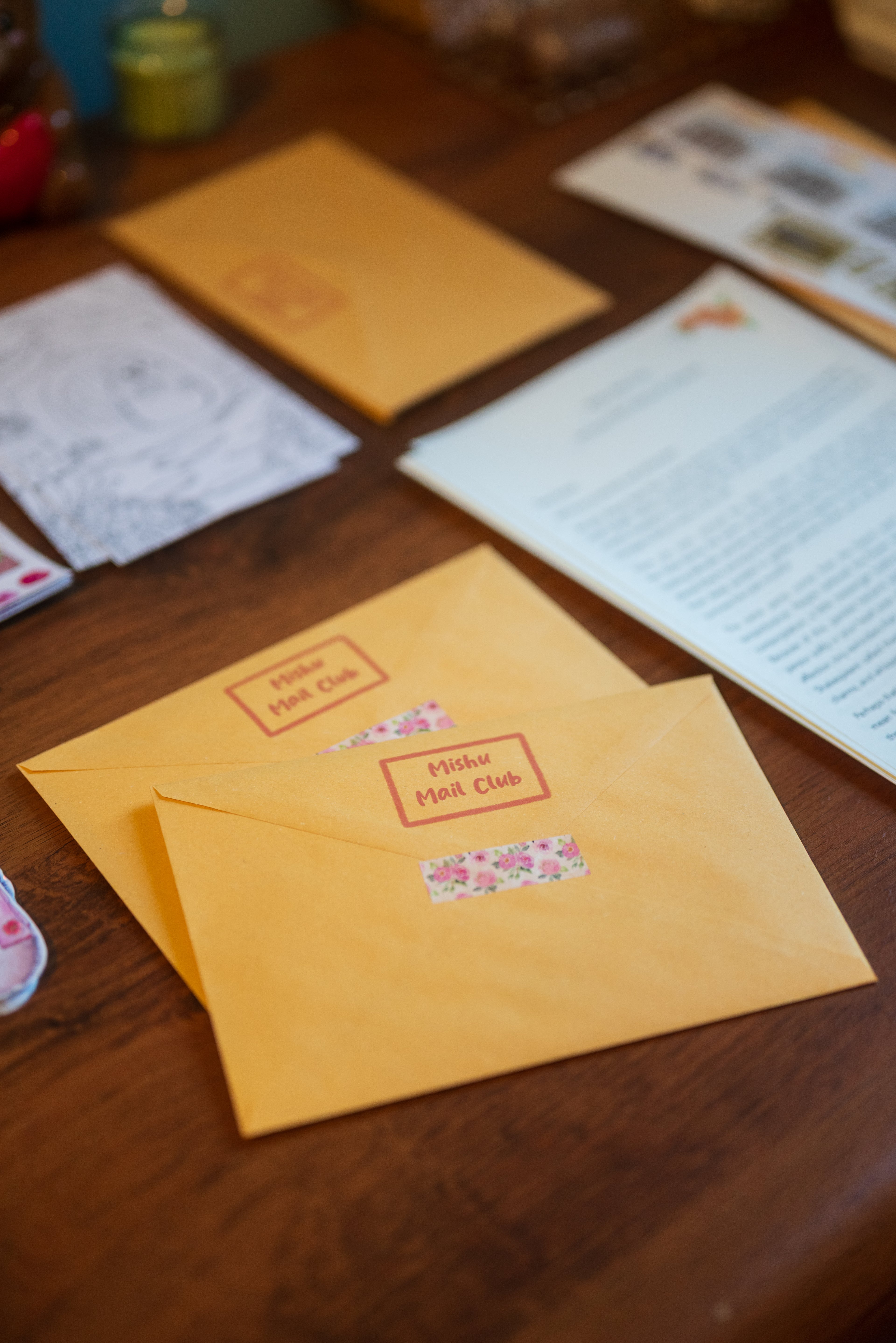 Yellow envelope with floral design and text on a wooden surface with other envelopes and papers.