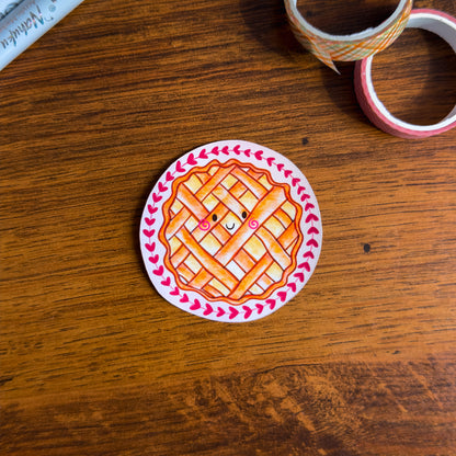 Circular sticker of a pie with a lattice top on a wooden surface