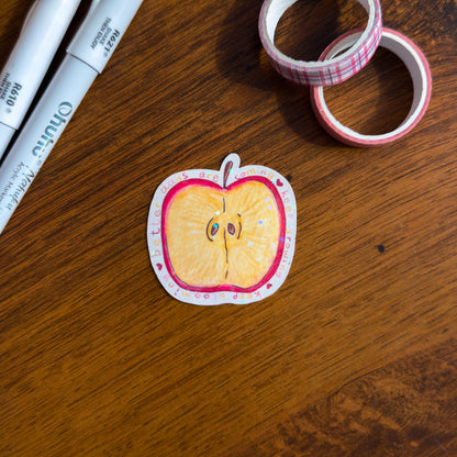 A hand-illustrated apple slice die cut sticker with holographic glitter lamination. Surrounded by the phrase "better days are coming, keep growing, keep blooming on a wooden surface