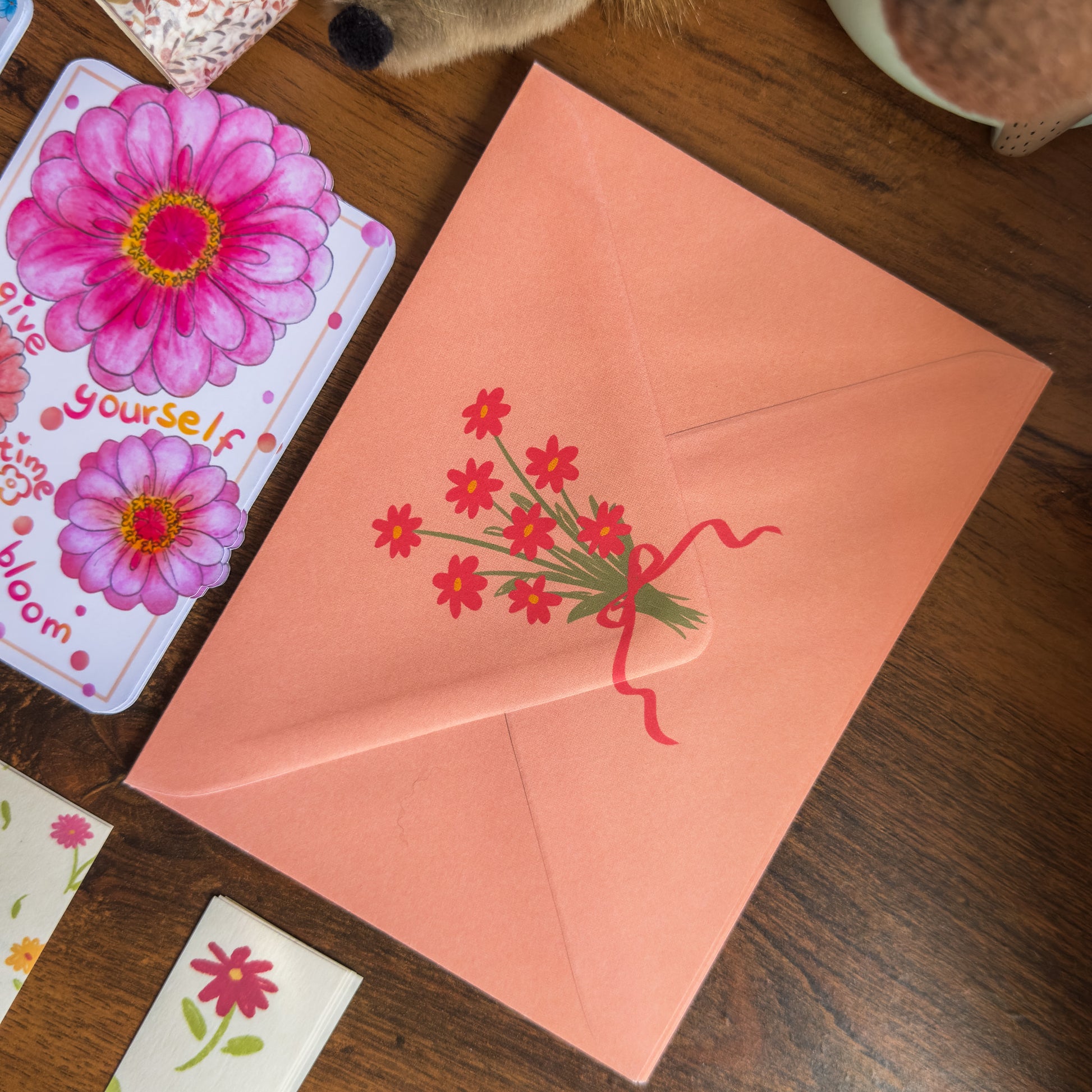Pink envelope with floral design on a wooden surface with cards featuring flowers.